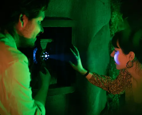 Two players shining a torch into a wall compartment